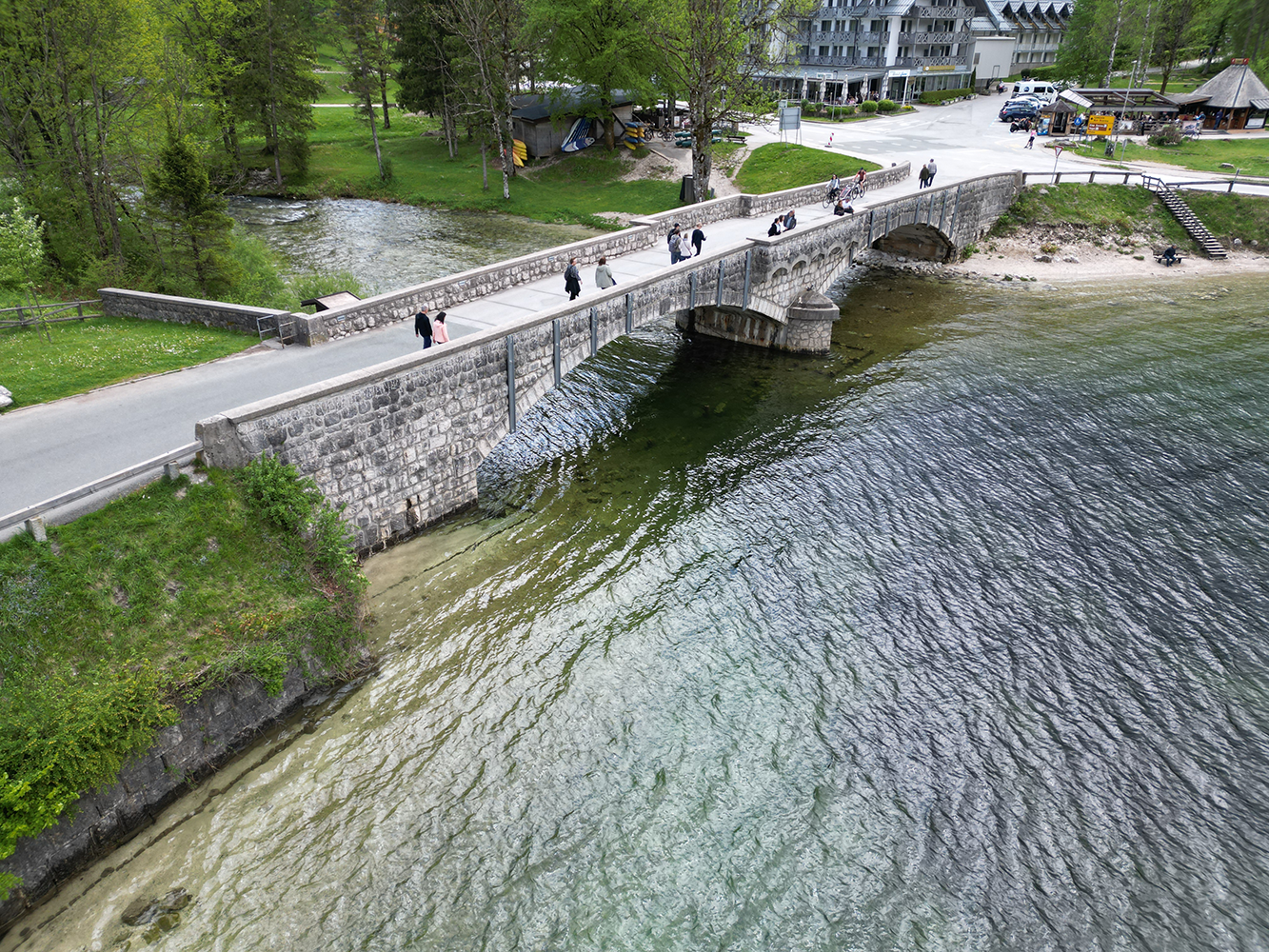 Aerial view of Cerkev Sv. Janeza Krstnika (Church of St. John the Baptist) with a bridge spanning a nearby river, surrounded by lush greenery.