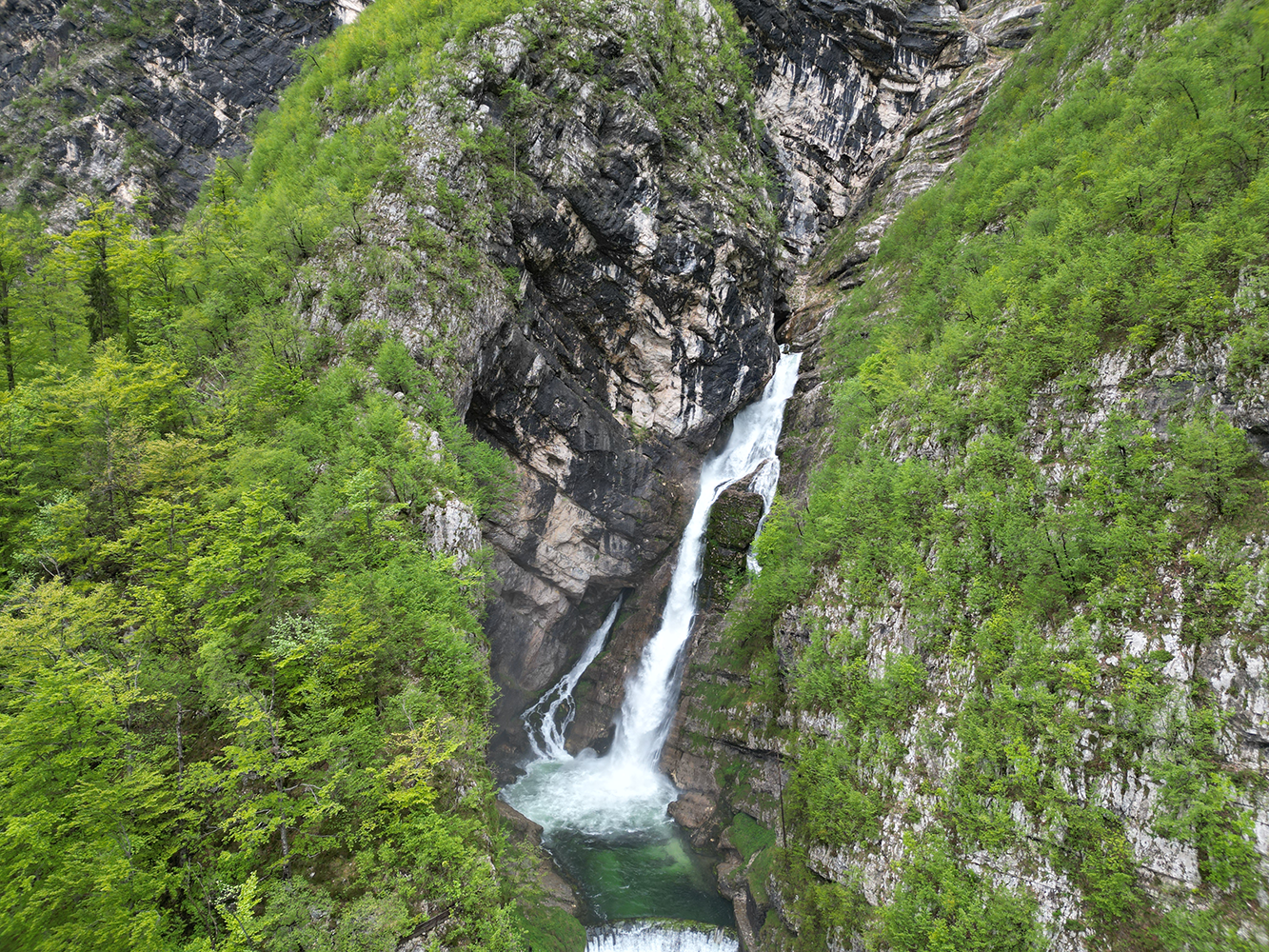 Distant view of Savica Waterfall surrounded by lush greenery and rocky cliffs.