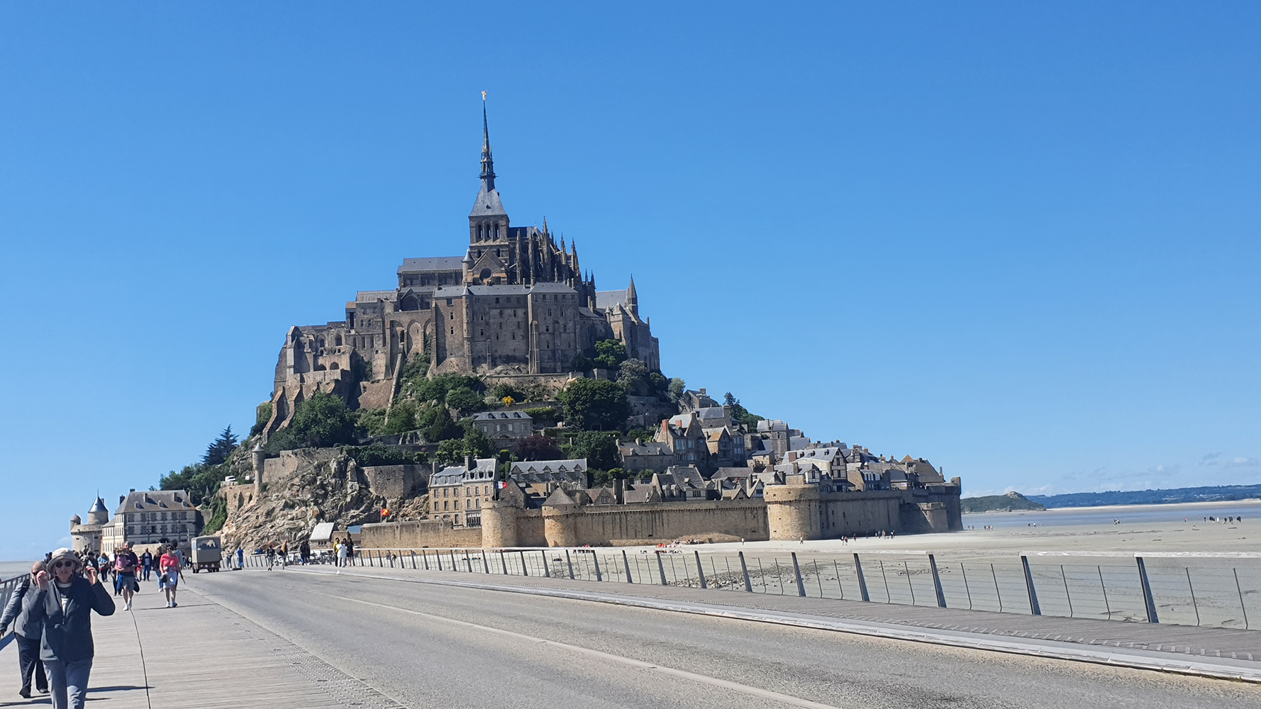 A breathtaking view of Mont Saint-Michel emerging on the horizon as seen from the approach, surrounded by the vast expanse of the tidal flats.