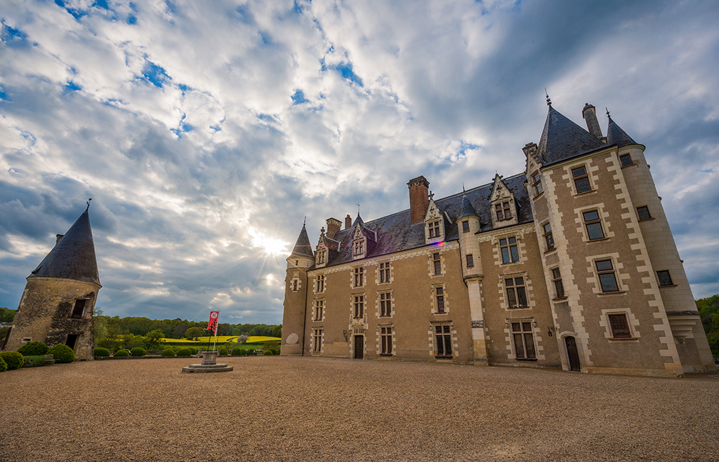 Exterior view of the entrance to Château de Montpoupon, surrounded by lush greenery and historic architecture.