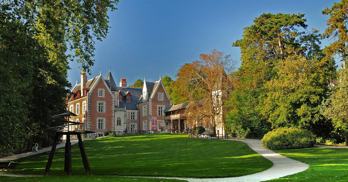 Exterior view of the entrance to Château du Clos Lucé, surrounded by vibrant flowers and lush greenery.