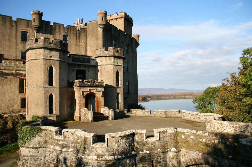 Dunvegan Castle on the Isle of Skye, featuring its historic stone architecture, lush surrounding gardens, and a scenic view of the adjacent loch.