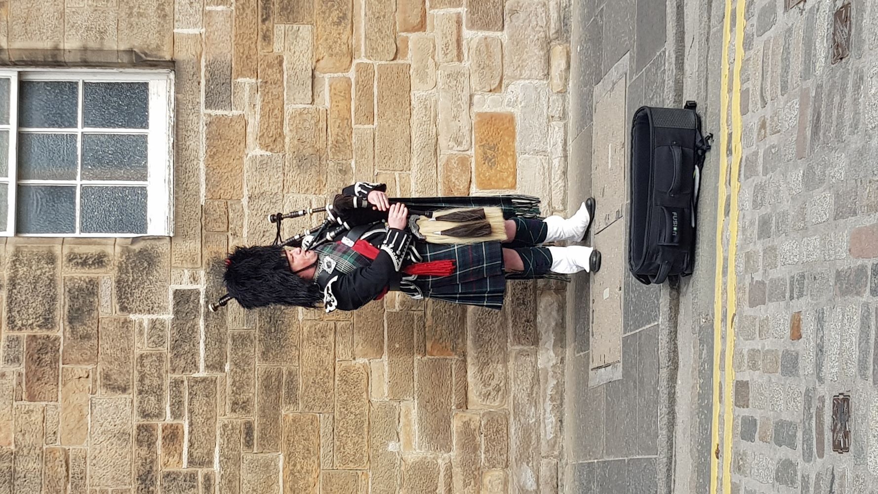 Scottish bagpipe player in traditional attire performing on a street in Edinburgh.