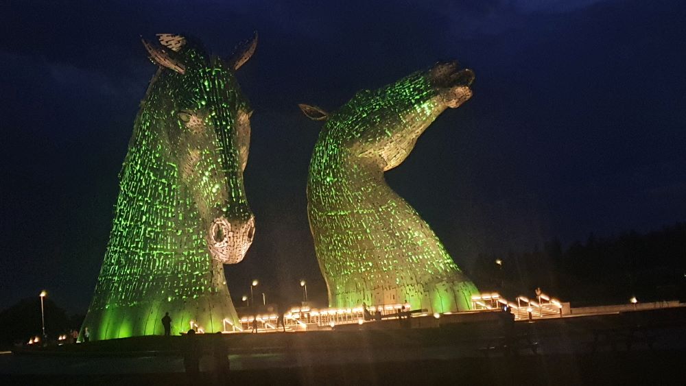 The Kelpies sculptures illuminated at night with colorful lights.
