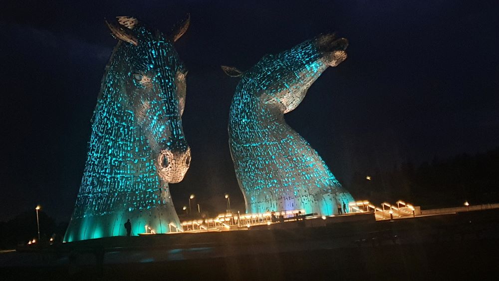 The Kelpies sculptures illuminated at night with colorful lights.