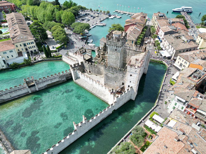 Aerial view of Castello Scaligero di Sirmione, a historic fortified castle surrounded by water in a scenic, picturesque setting.