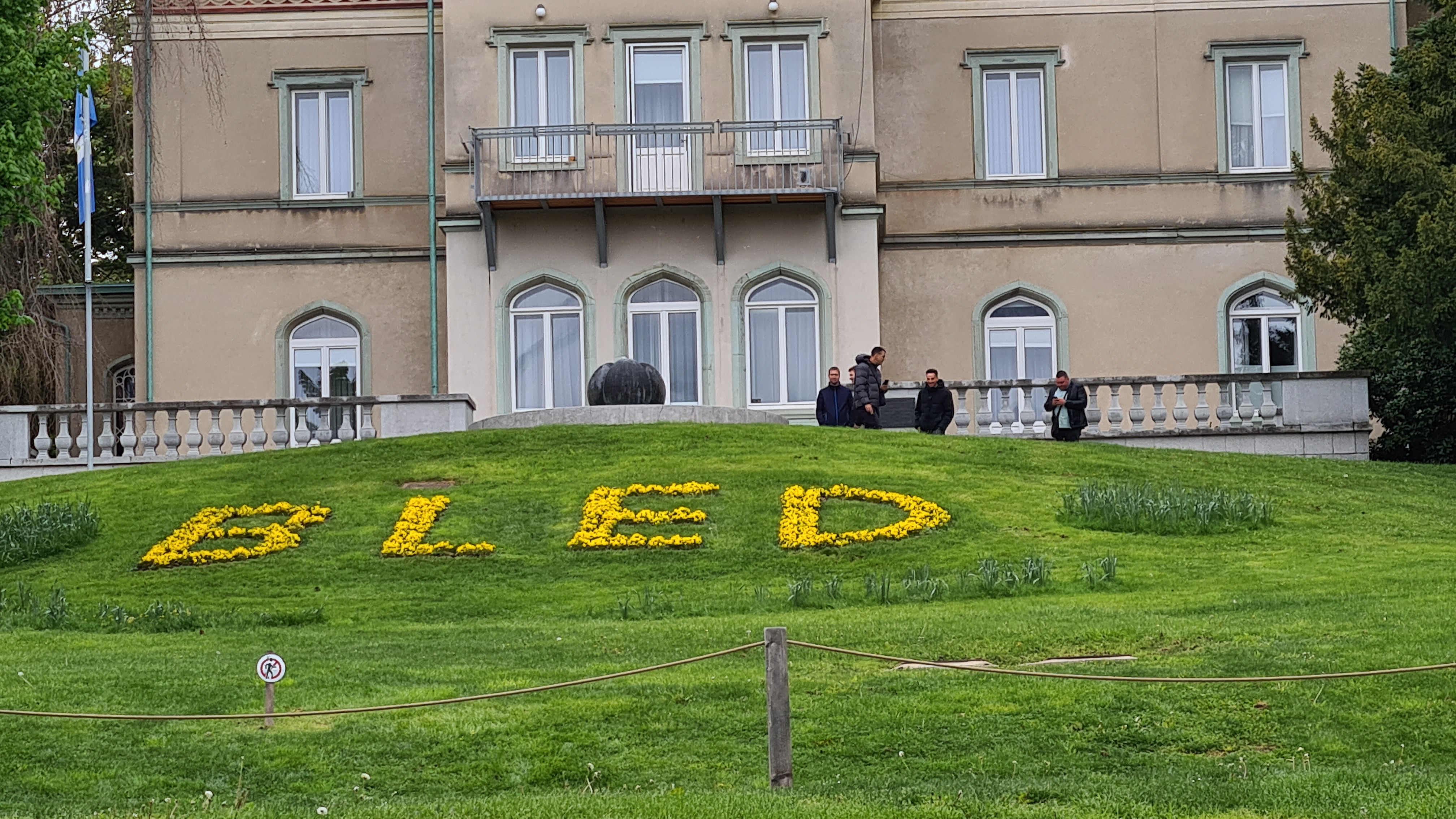 Flowers arranged to spell out 'Bled' near the shore of Lake Bled, with the serene waters and lush surroundings in the background.