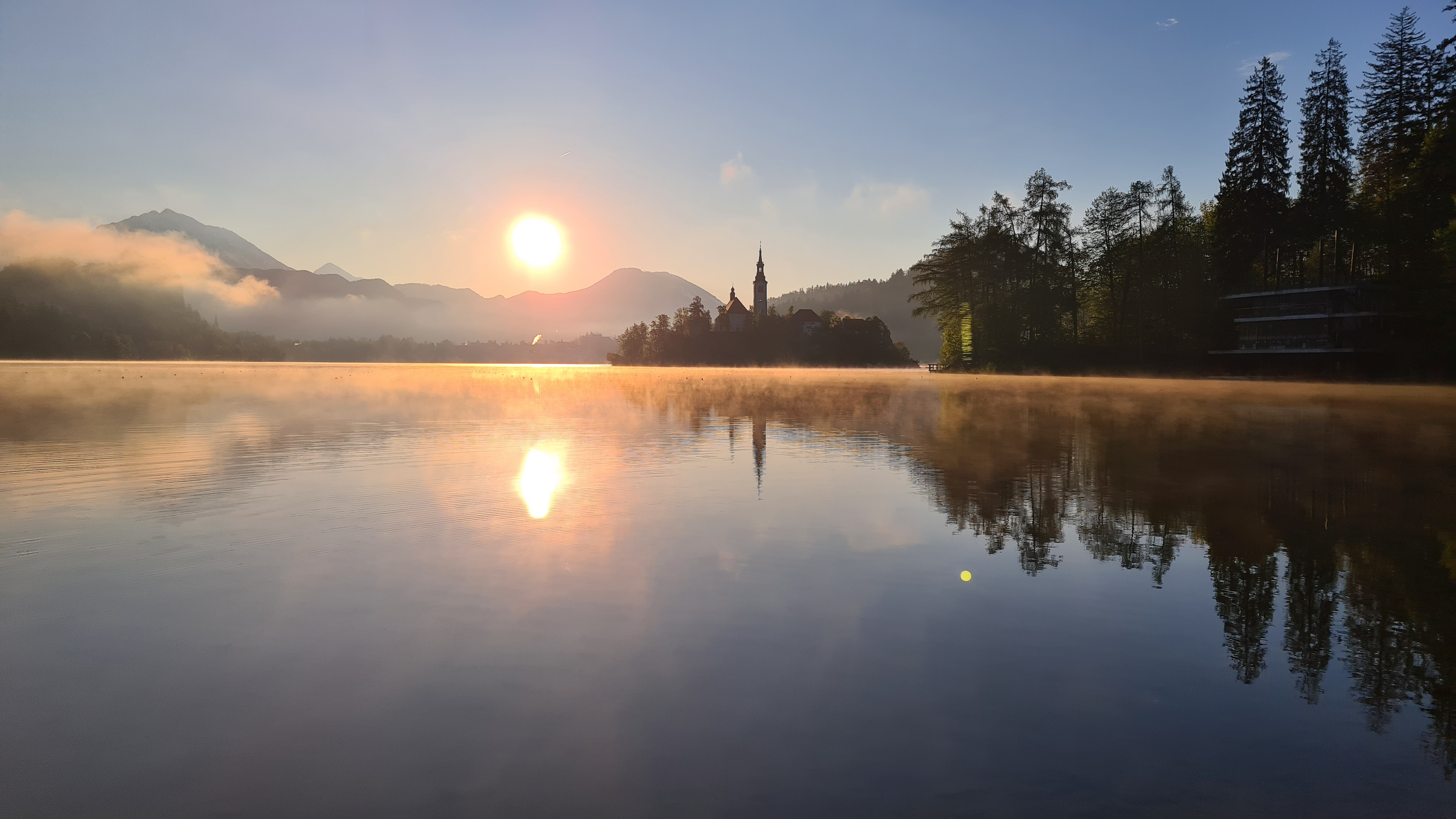 Dawn at Lake Bled, with soft morning light illuminating the tranquil waters and surrounding mountains.