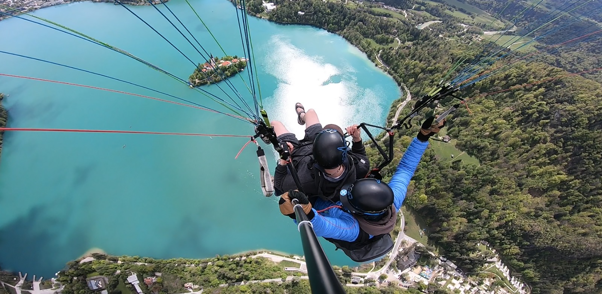 Aerial paragliding view of Bled Island, showcasing the island's lush greenery and the Church of the Assumption surrounded by the crystal-clear waters of Lake Bled.
