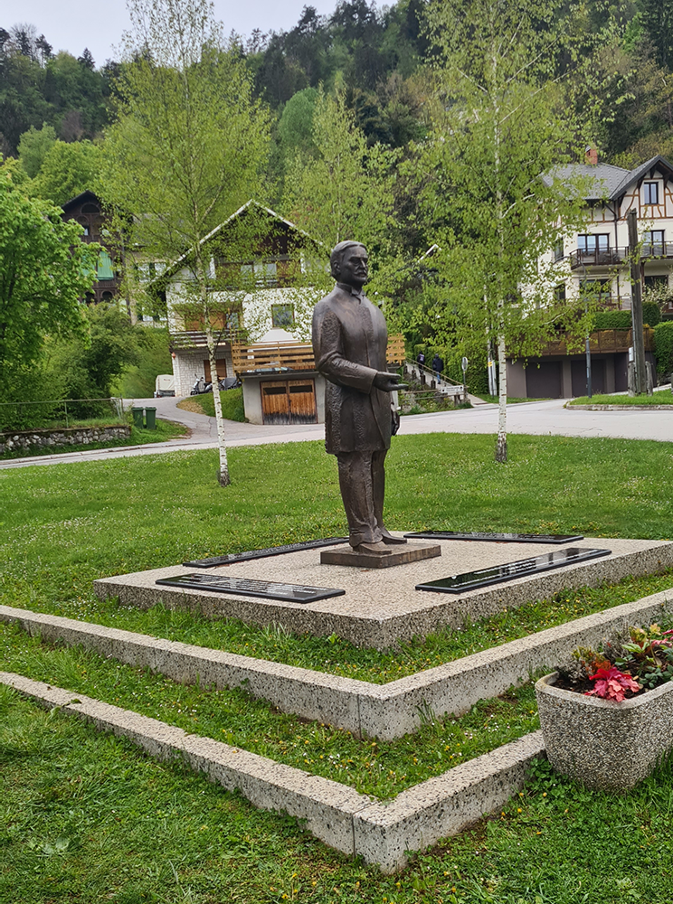 Statue on Bled Island with the Church of the Assumption in the background, surrounded by lush greenery.