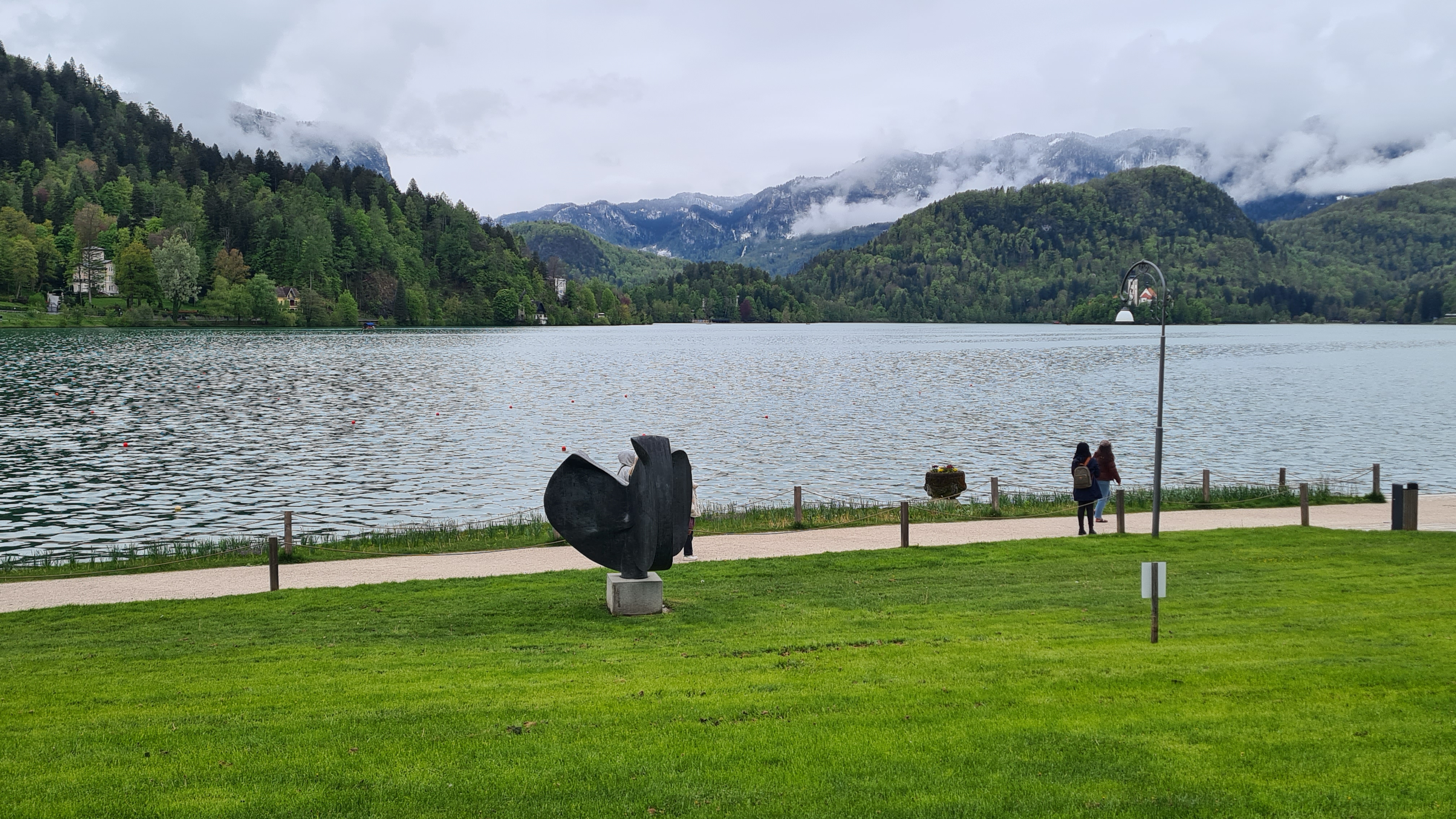 Statue on Bled Island with the Church of the Assumption in the background, surrounded by lush greenery.