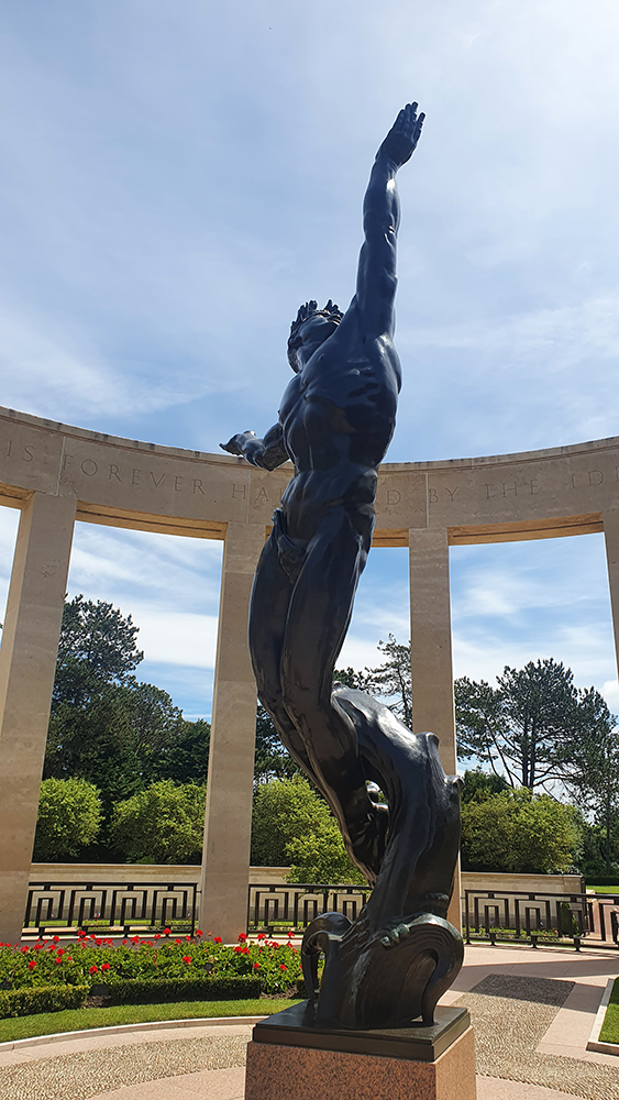 A solemn statue standing amidst the graves at Normandy American Cemetery, symbolizing honor and remembrance for the fallen soldiers of World War II.