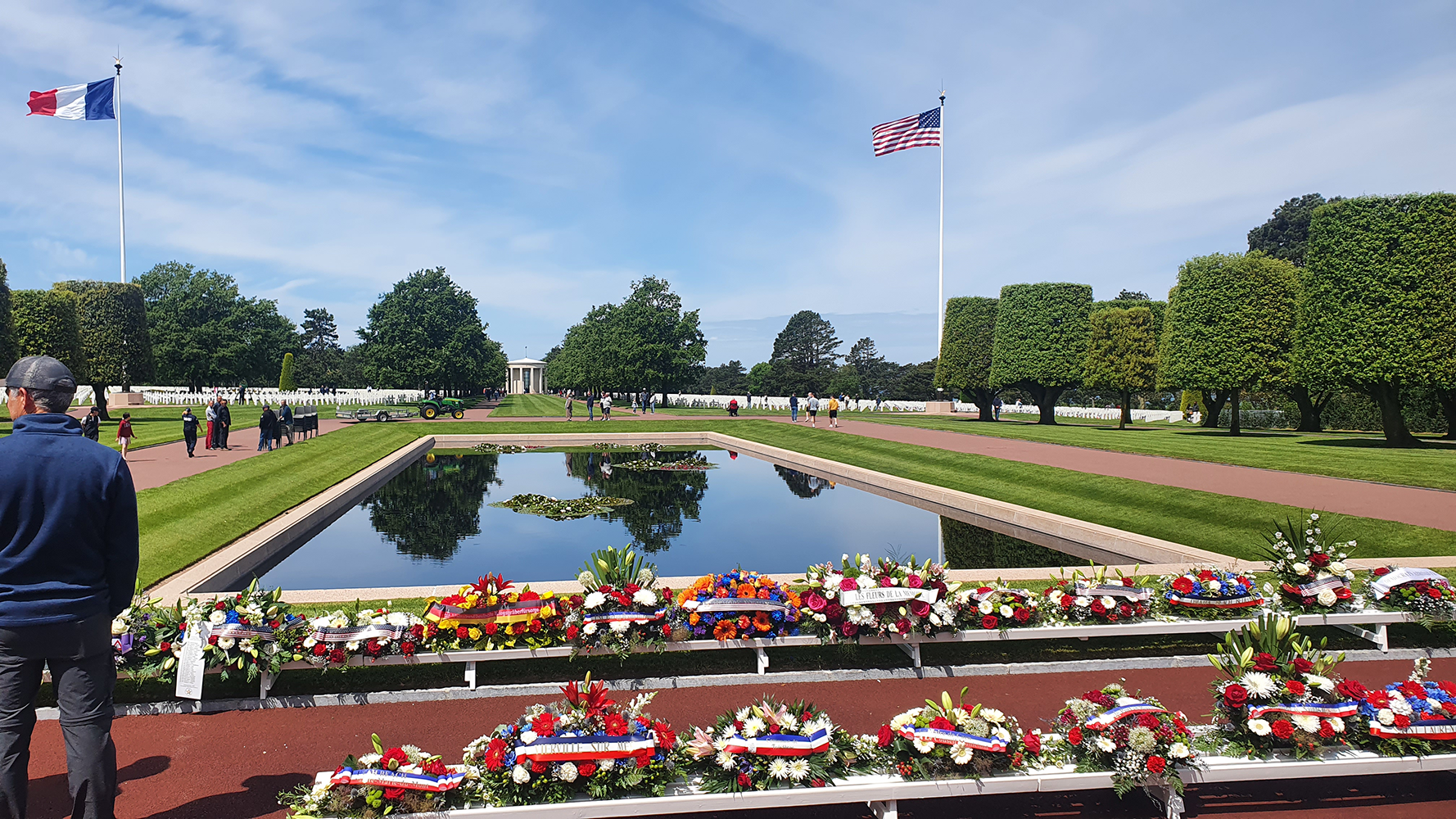 Discover the solemn beauty of the Normandy American Cemetery, featuring a peaceful pond before rows of white crosses commemorating the sacrifice of American soldiers in World War II.