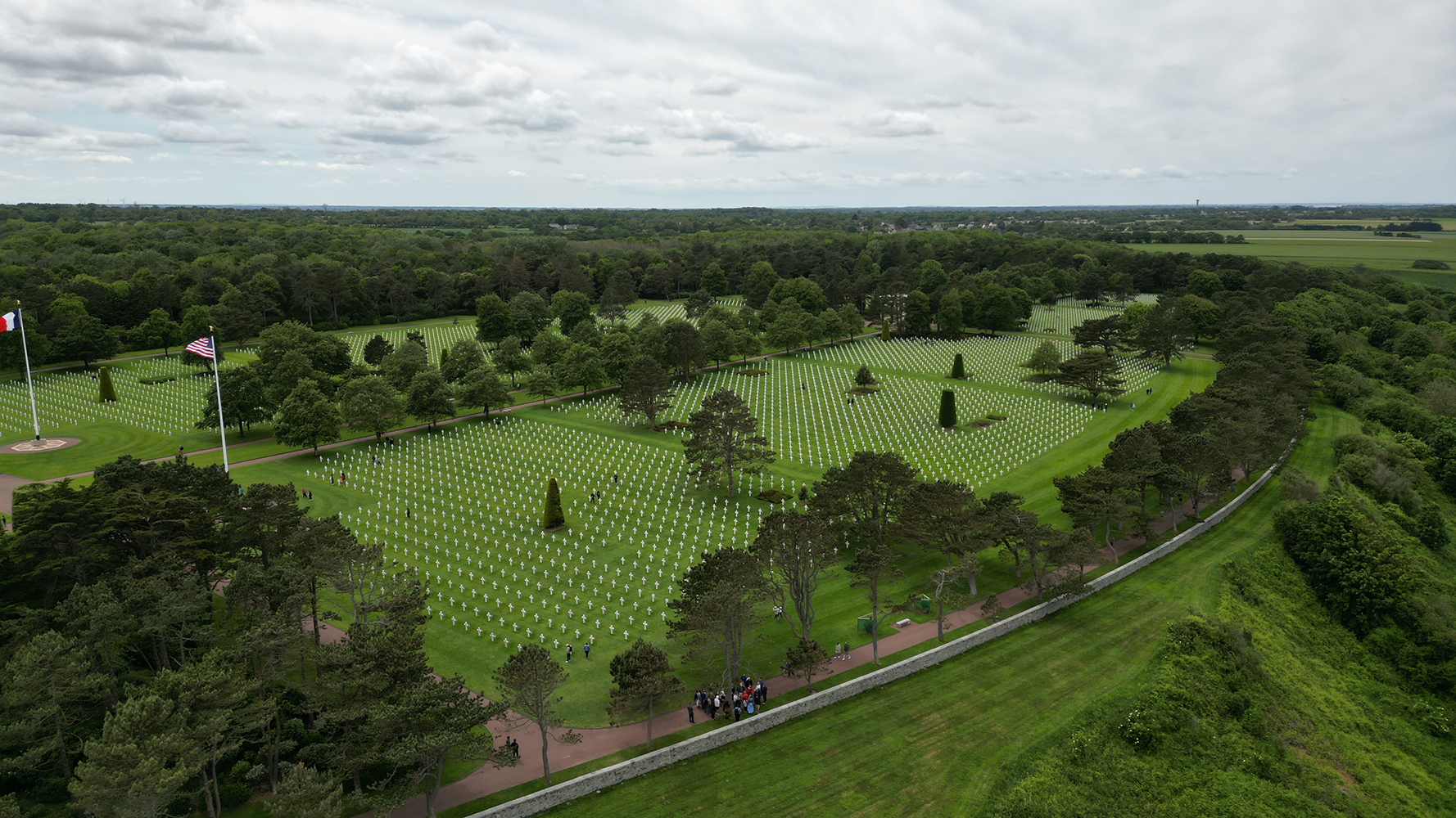 Experience the solemn sight of the Normandy American Cemetery from the air, showcasing the orderly rows of white crosses that honor the bravery and sacrifice of American soldiers.