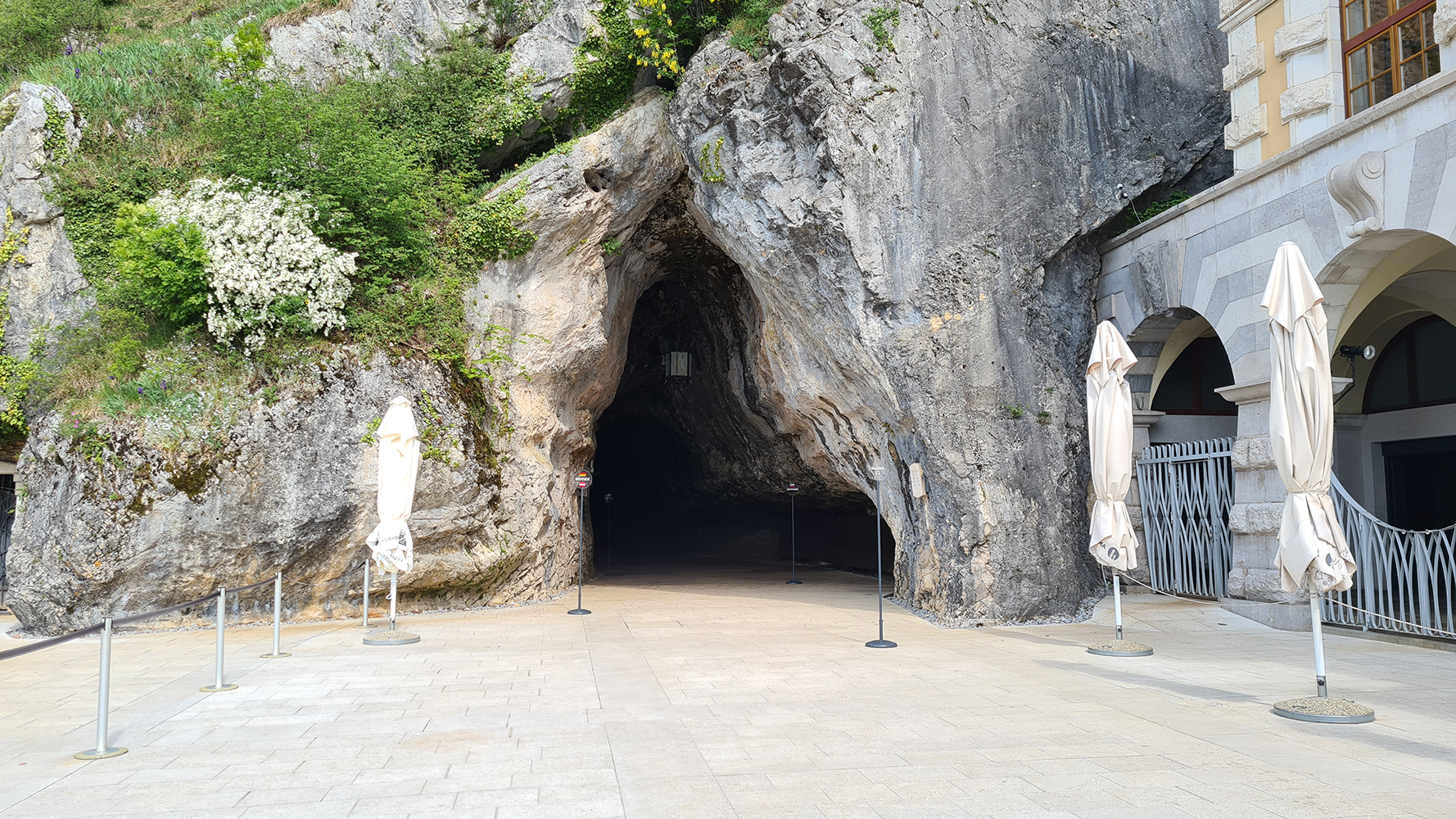 Entrance to Postojna Cave, with visitors entering the cave's mouth surrounded by lush greenery.
