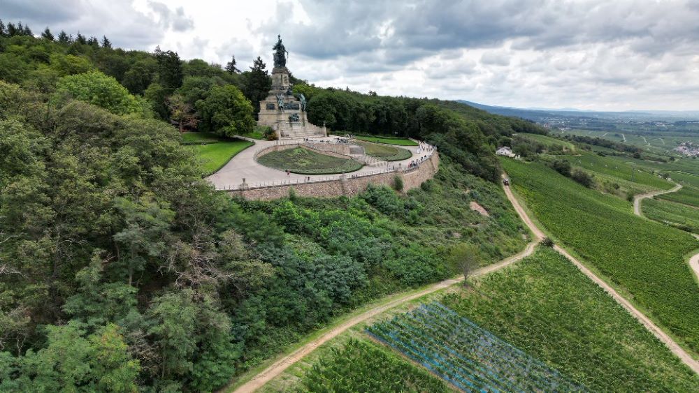 Distant view of the Niederwald Monument, standing tall atop a hill with the Rhine River and surrounding landscape in the background.