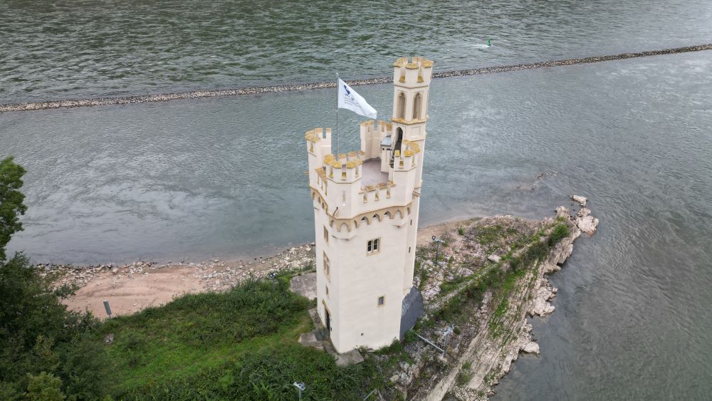 Aerial view of the Mouse Tower (Mäuseturm) situated on a small island in the Rhine River, surrounded by water and picturesque landscape.