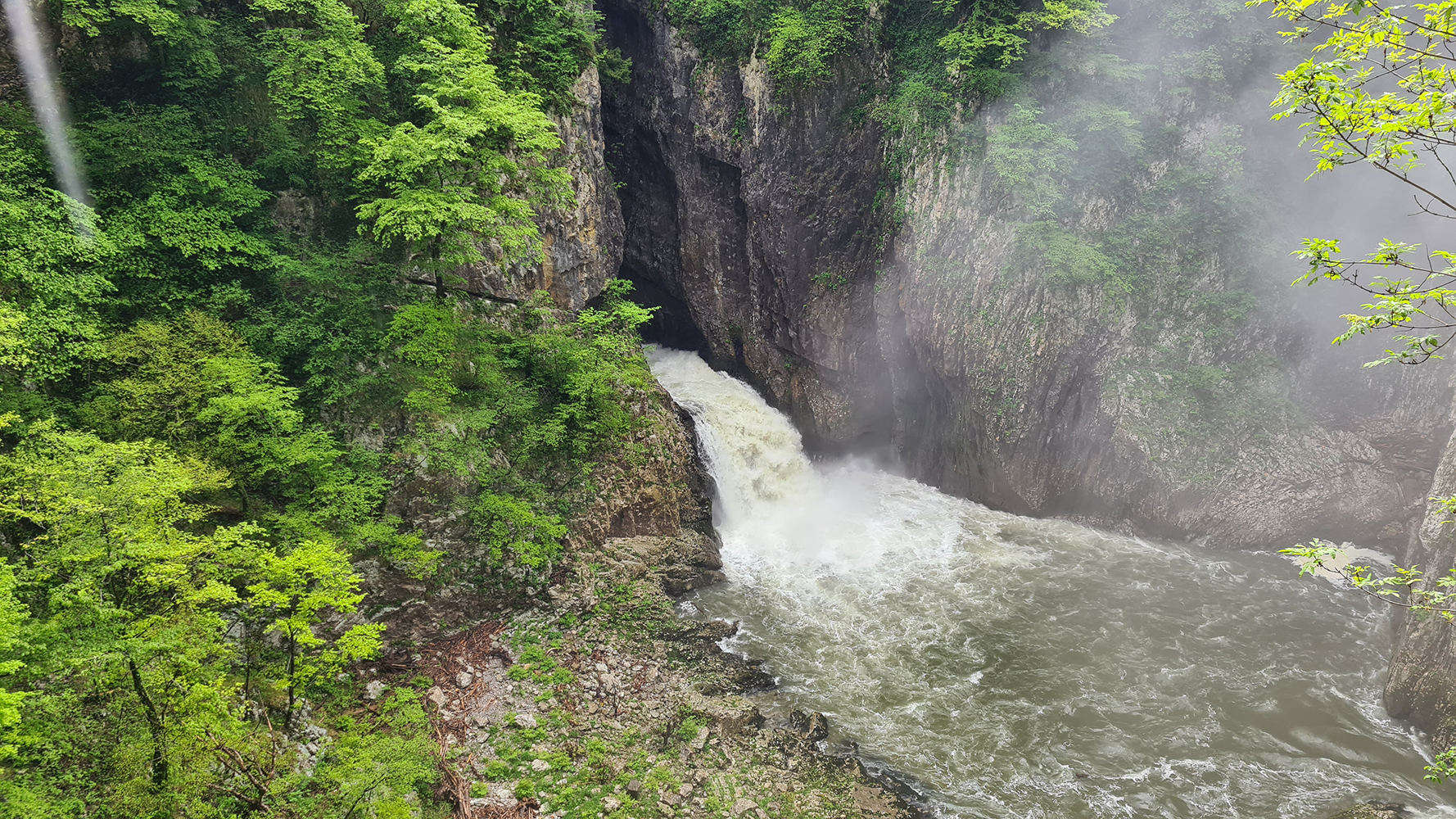 Exterior view of Skocjan Caves, with the Reka River flowing through the lush landscape surrounding the entrance.