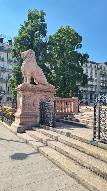 Lion statue in a park surrounded by trees and open sky, serving as an artistic monument