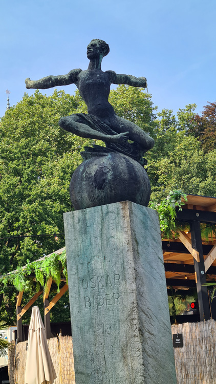 Outdoor statue of a man holding a spear, surrounded by trees and a clear sky at Bern Spielplatz