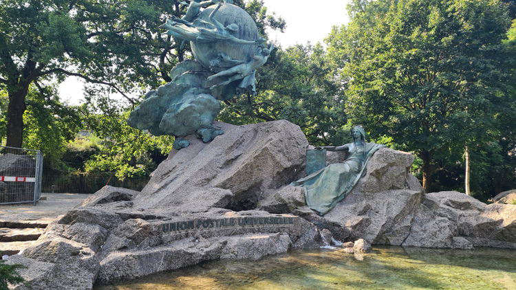 Statue of a person on a rock in a Bern park, surrounded by trees, grass, and a clear sky