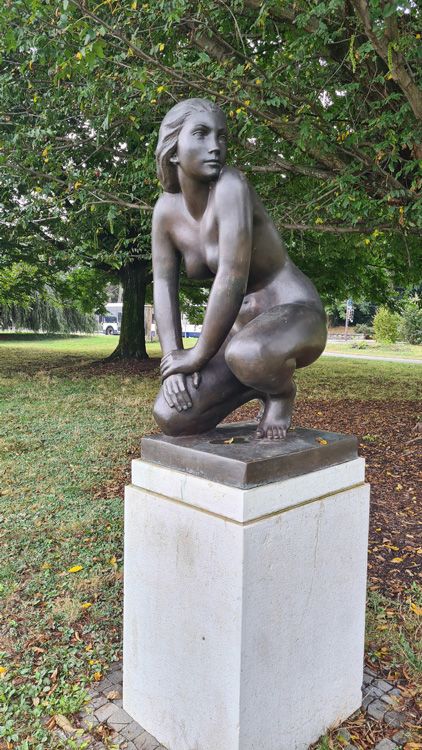 Outdoor bronze statue of a woman in Geneva, surrounded by trees, grass, and classical architecture